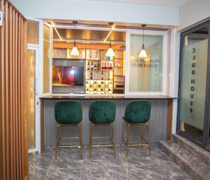 Eine Bar mit drei grünen Barhocker, einem Fernsehbildschirm und Flaschenregalen.