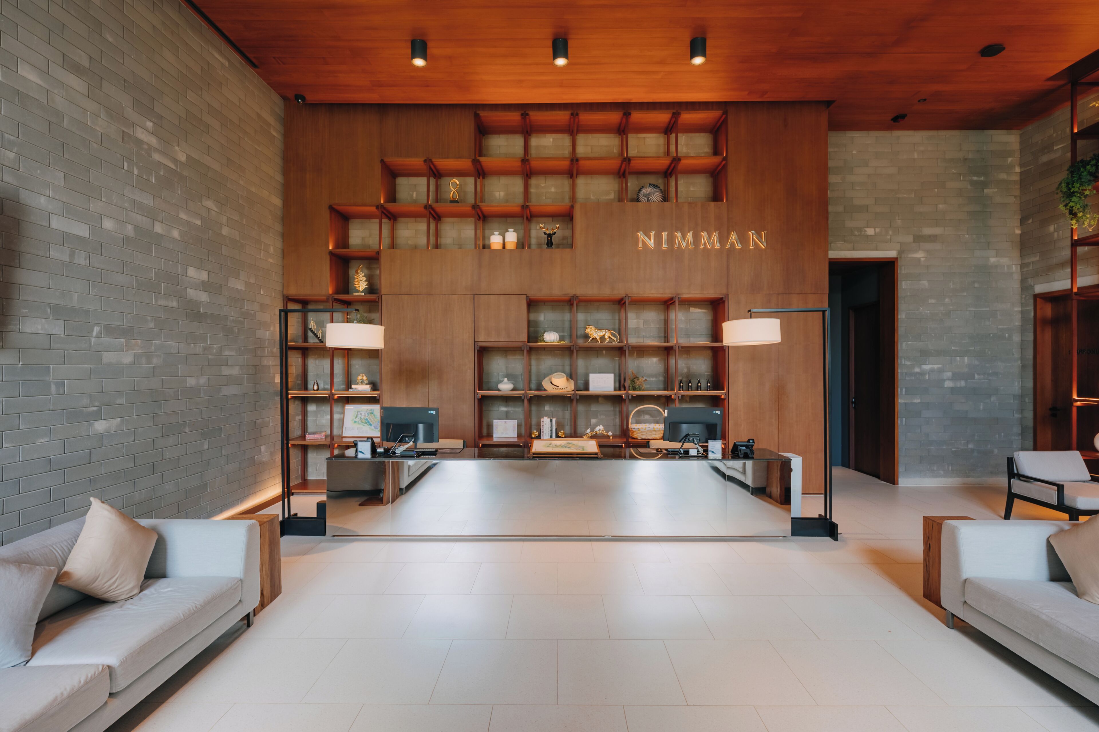 A modern lobby with a brick wall, wooden shelving displaying various items, and two sofas.