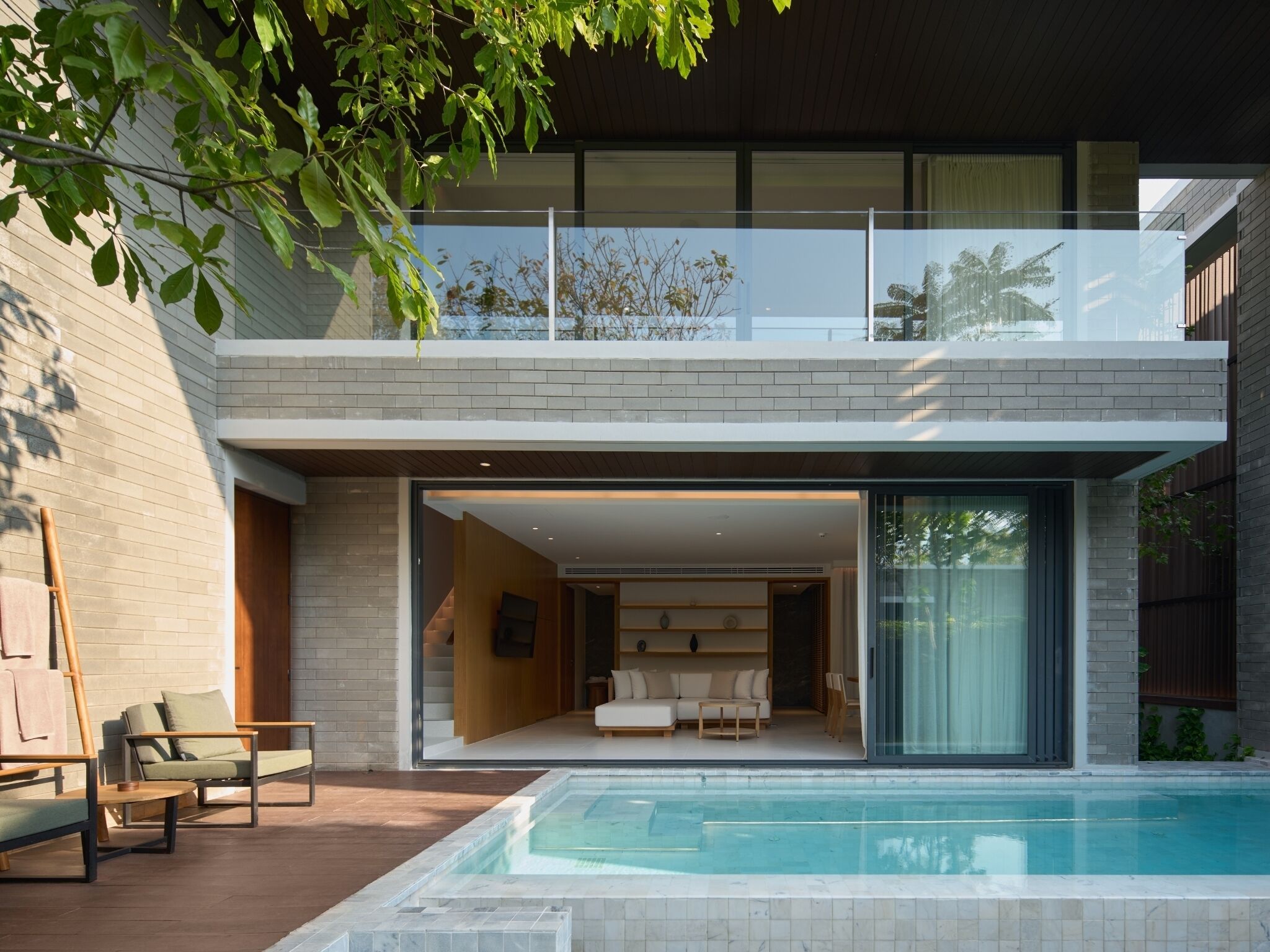 A modern two-story house with a glass balcony, a swimming pool, and a well-lit interior.