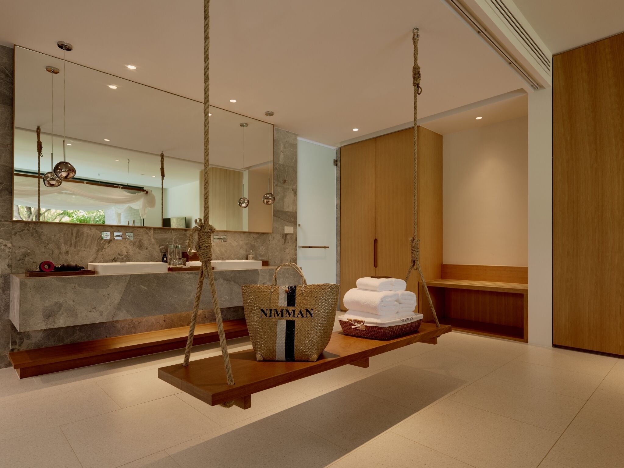 A modern bathroom with a marble sink, wooden swing chairs, and a large mirror.