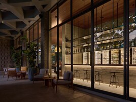 Un moderno bar con amplios ventanales, asientos y una pared de ladrillo.