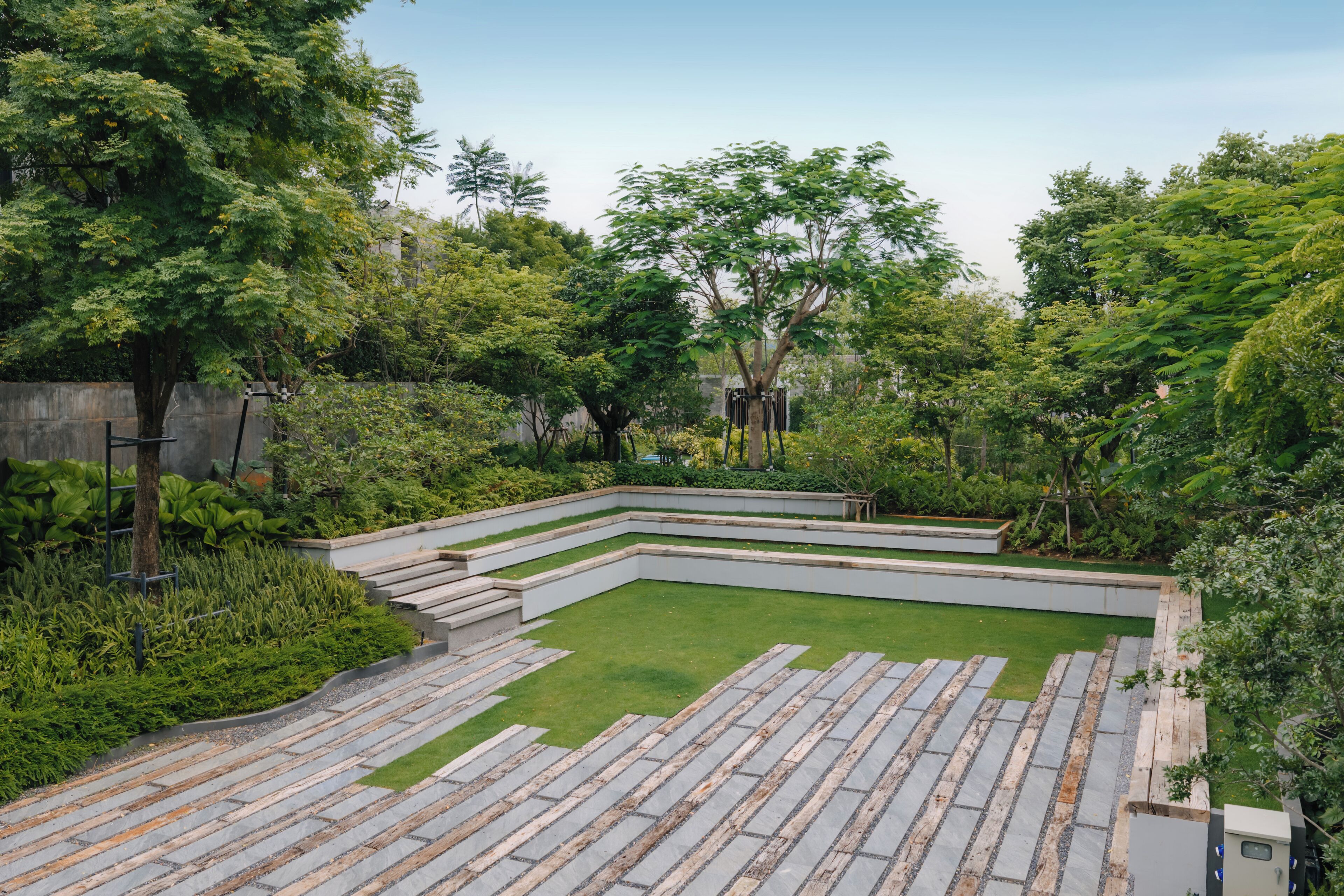 Un jardín ajardinado con césped central, senderos de piedra y diversas especies de árboles.
