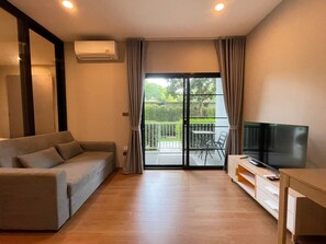 A modern living room with a sofa, a TV, and a sliding glass door leading to a balcony. - The Title Rawai Aparthotel by HSS (Rawai)