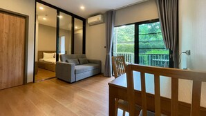 Ein modernes Hotelzimmer mit Holzboden, einem grauen Sofa, einem Holztisch und einem Balkon mit Blick auf Grünflächen.