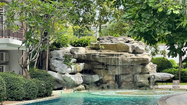 Ein Pool mit Wasserfall, umgeben von üppiger Vegetation und einem mehrstöckigen Gebäude.