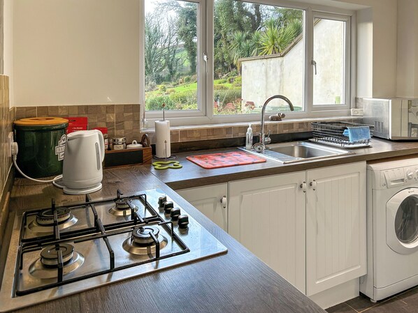 A modern kitchen with a gas stove, a washing machine, and a window with a view of greenery.