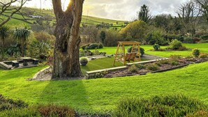 Ein Garten mit Schaukel, Steinbank und einem großen Baum.