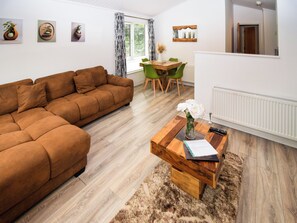 Ein modernes Wohnzimmer mit einer braunen Couch, einem Couchtisch mit einer Vase und einem Essbereich mit grünen Stühlen.