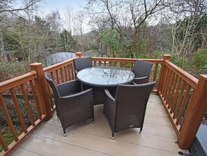 Eine Holzterrasse mit einem runden Glastisch und Korbstühlen.
