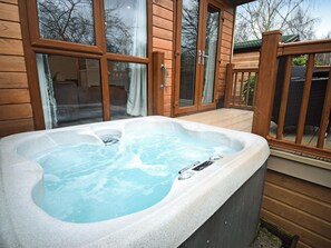Ein Whirlpool in einem Holzdeckbereich mit Glastüren und Blick auf Bäume.