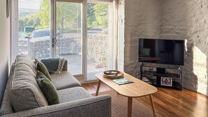 A living room with a sofa, a television on a stand, and a sliding glass door leading to a parking area. - 2 bedroom accommodation in Buckden, near Skipton (Buckden, near Skipton)