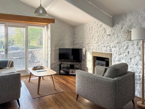 A living room with a stone wall, a fireplace, a television, and a sofa. - 2 bedroom accommodation in Buckden, near Skipton (Buckden, near Skipton)