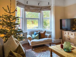 A cozy living room with a Christmas tree, a comfortable sofa, a television, and a wooden cabinet.