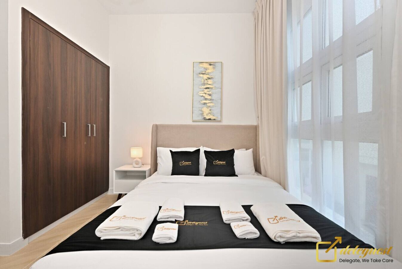 Ein Hotelzimmer mit großem Kleiderschrank, einem Bett mit zwei Kissen, einem Nachttisch mit Lampe und Handtüchern auf dem Bett.