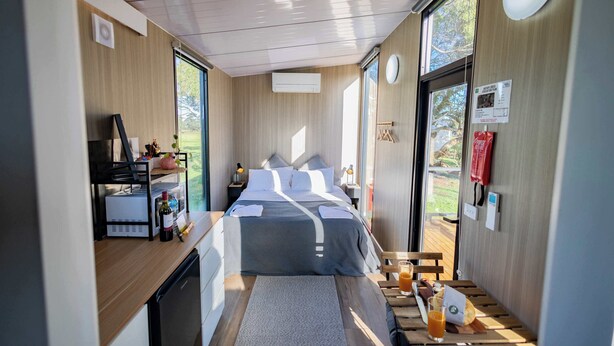 Una habitación compacta con cama, escritorio pequeño, refrigerador y ventana que ofrece vistas al exterior.