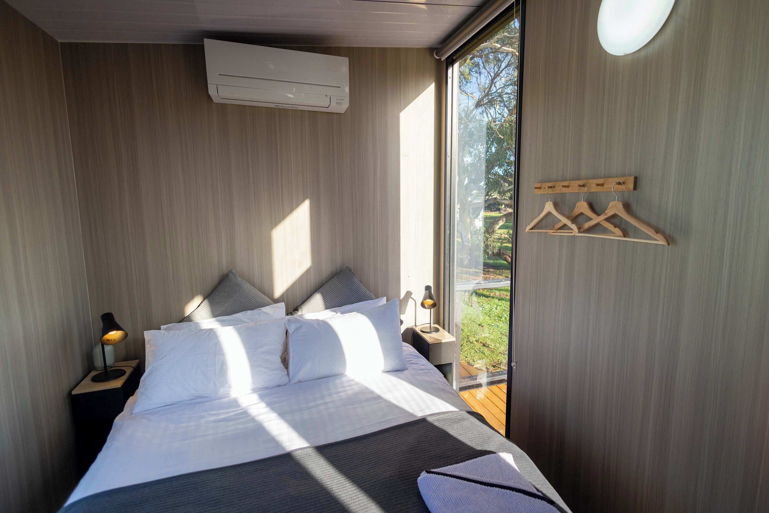 Une chambre moderne avec un lit, des tables de chevet, un climatiseur et une vue sur la verdure.
