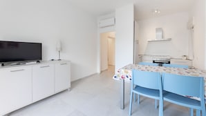 Een moderne keuken met een kookplaat, oven en magnetron. Er staat een eettafel met stoelen en een televisie op een kast.