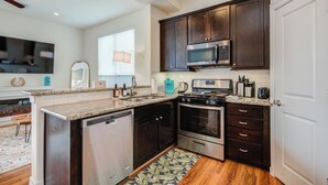 A modern kitchen with dark wood cabinets, stainless steel appliances, and a granite countertop. - Famous Houston Heights Home & Game Room (Houston)