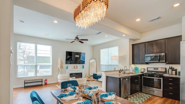 A modern kitchen with dark cabinets, stainless steel appliances, and a dining area with blue chairs and a wooden table set for six. - Famous Houston Heights Home & Game Room (Houston)