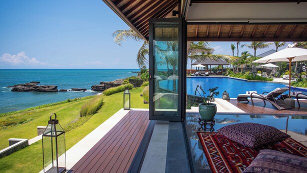 Una villa moderna con una porta in vetro che si apre su una piscina privata, con vista sulla costa rocciosa e sull'oceano.
