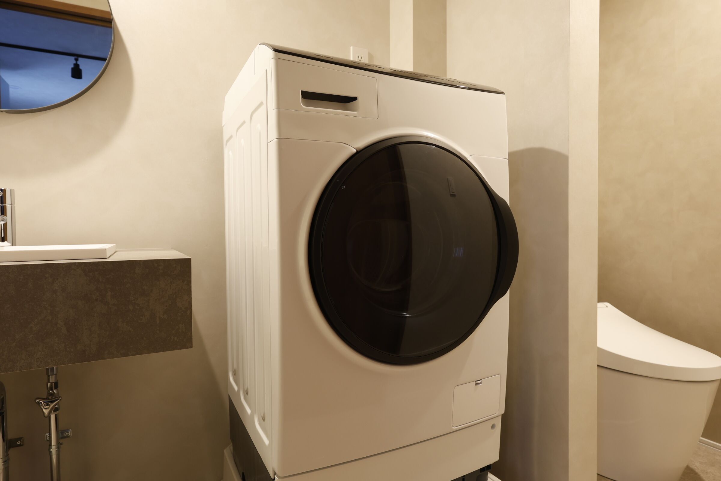 A compact, modern laundry room with a front-loading washing machine, a toilet, and a small sink.