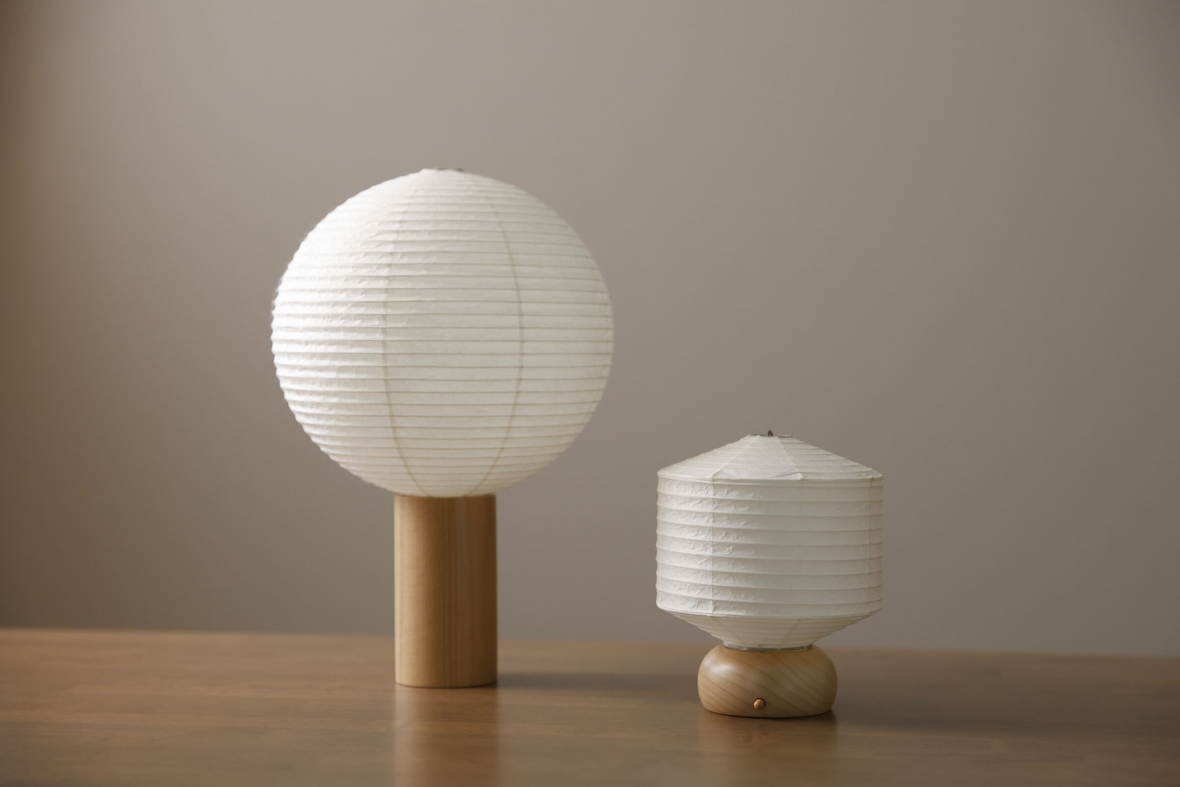 Two paper lanterns on a wooden table against a plain background.