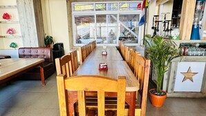 A dining area with a long wooden table and chairs, a bar area with a star decoration, and a large window providing a view of the outside. - Hotel Prem Durbar (Bageshwori)