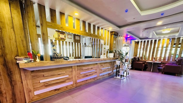 A reception desk with a wooden finish, a statue, and framed certificates. There are potted plants and a seating area with sofas. - Hotel Prem Durbar (Bageshwori)