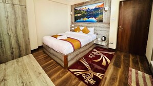 A bedroom with a wooden bed, a large painting of a mountain landscape, a chandelier, and a wooden wardrobe. - Hotel Prem Durbar (Bageshwori)
