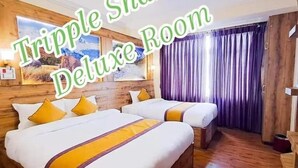 A triple sharing deluxe room with wooden walls, a large bed, and a window with purple curtains. - Hotel Prem Durbar (Bageshwori)