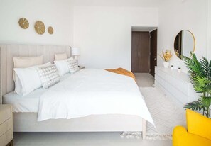 A modern bedroom with a bed, bedside tables, a dresser, a mirror, and decorative wall art. - Lagoon View Apartment w/ Pool, Beach & Gym Access (Ajmal Makan)
