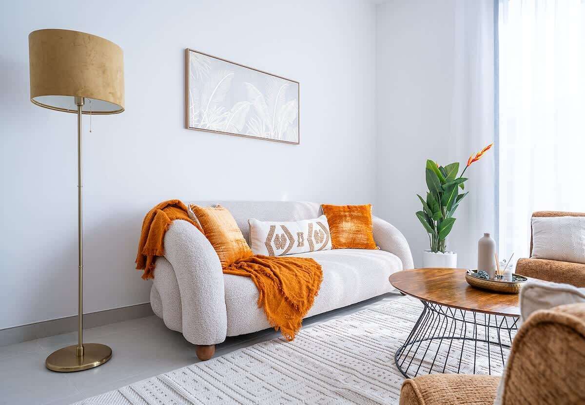 Uma sala de estar moderna com um sofá branco, uma mesa de centro redonda, um abajur e um quadro na parede.