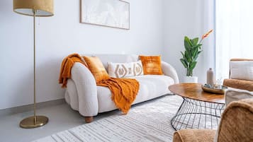 Uma sala de estar moderna com um sofá branco, uma mesa de centro redonda, um abajur e um quadro na parede.