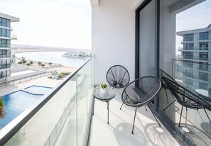 A balcony with a pool, two chairs, and a view of a body of water and buildings.