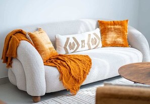 A white sofa with a textured throw blanket and two pillows, one with a geometric pattern and another with a solid color.