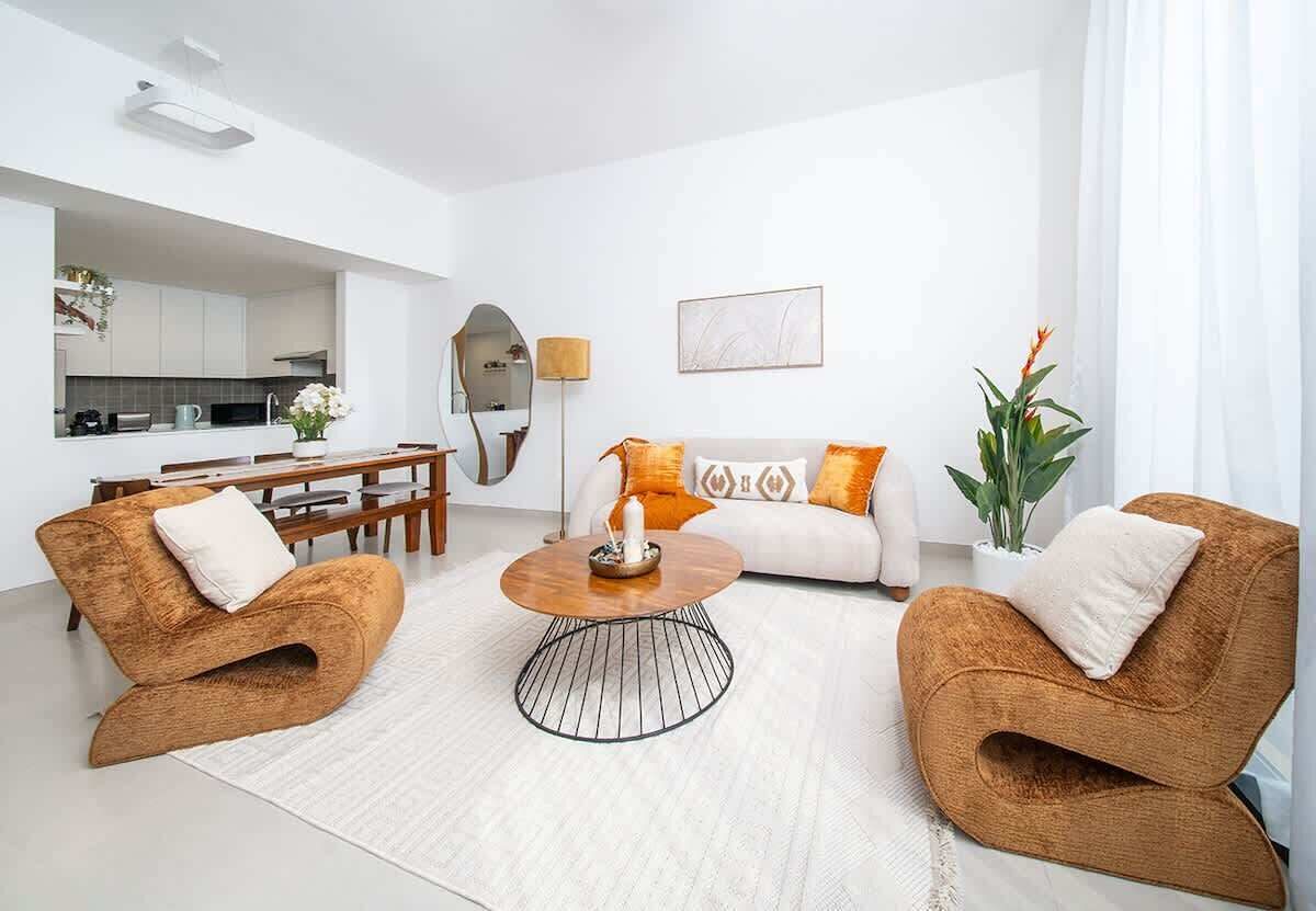 Een moderne woonkamer met een bank, twee fauteuils, een salontafel en een eethoek met een tafel en stoelen.