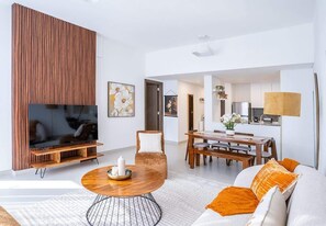 Una sala moderna con un televisor de pantalla plana, una mesa redonda, un sofá y una zona de comedor con una mesa y sillas de madera.