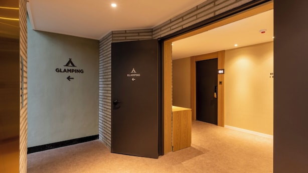A hotel corridor with directional signs for 'GLAMPING' and a wooden bench. - AVENUE S HOTEL (Siheung)