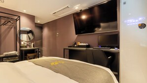 A hotel room with a bed, a desk with a computer, a TV mounted on the wall, and a mirror. - AVENUE S HOTEL (Siheung)