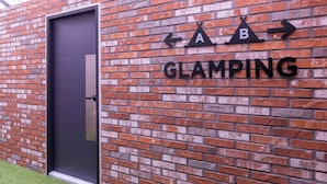 A brick wall with directional signs and the word "GLAMPING" indicating a camping area. - AVENUE S HOTEL (Siheung)