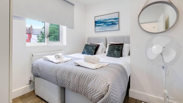 Un dormitorio con cama, ventana, espejo en la pared y ventilador de pie.