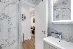 A bathroom with a marble floor, a white sink, a glass shower enclosure, and a marble-tiled wall. - West Hendon Apt with Parking 03 (London)