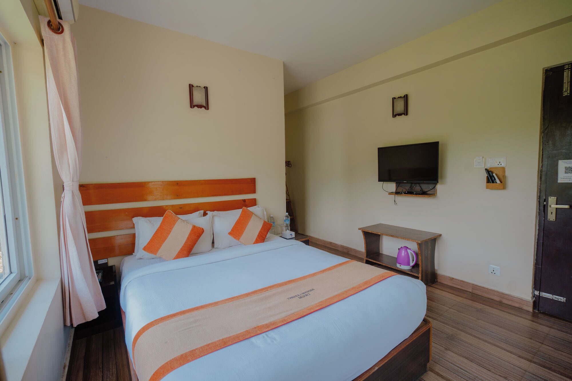 Una habitación de hotel con una cama, televisión, una mesita y una puerta.