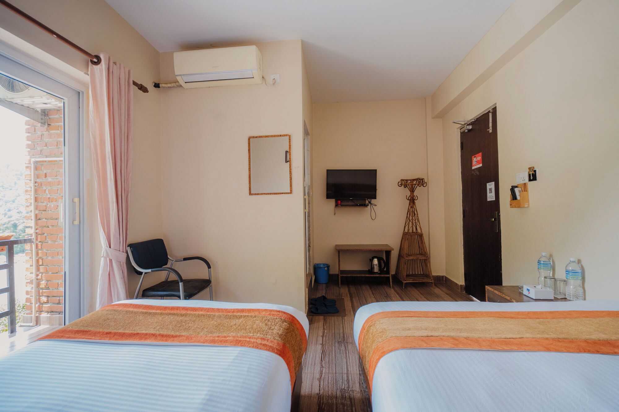 A hotel room with two beds, a TV, a chair, a small table, and a door.