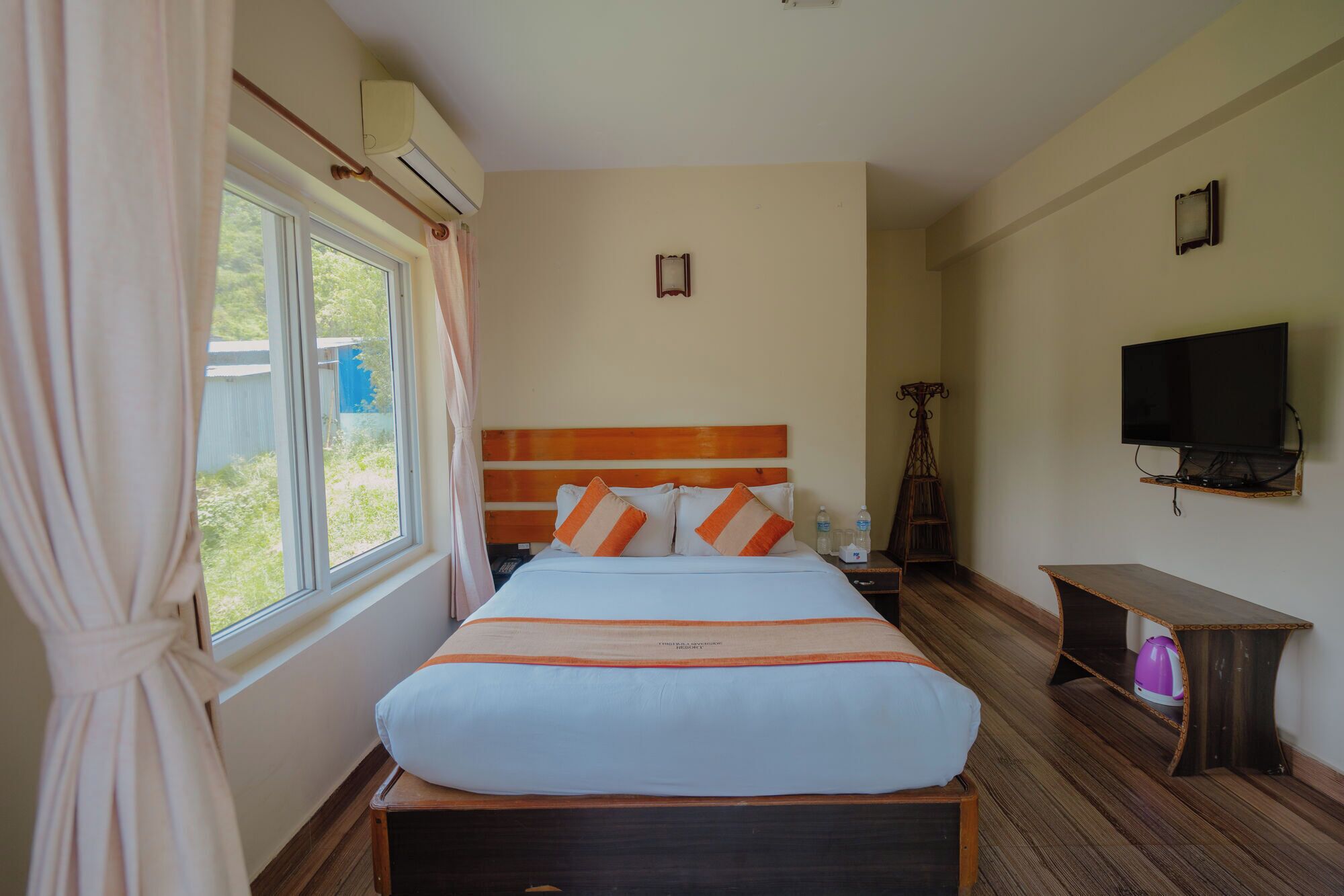 A hotel room with a large bed, a TV, a wooden nightstand, and a window with curtains.