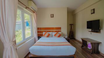 A hotel room with a large bed, a TV, a wooden nightstand, and a window with curtains.