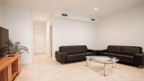 A modern living room with two leather sofas, a glass coffee table, and a wooden TV stand.
