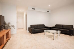 A modern living room with two leather sofas, a glass coffee table, and a wooden TV stand.