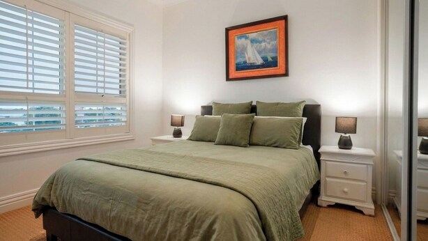 A bedroom with a bed, two bedside tables, a nightstand, a window with blinds, and a framed picture on the wall.