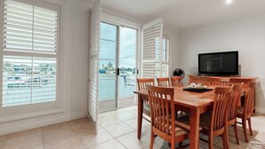 A dining area with a wooden table and chairs, a television, and a view of a marina through large windows.